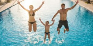 Family happily jumping into a swimming pool with perfectly clear, blue water.